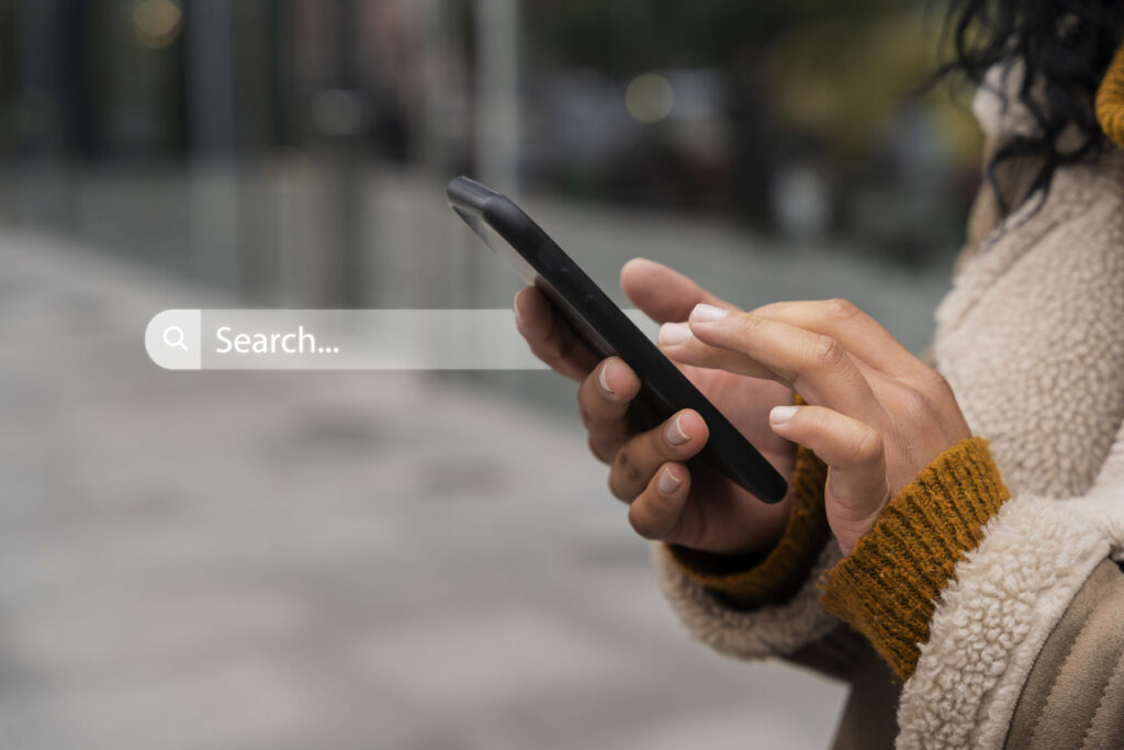 A woman holds a cell phone and a Google search field appears beside it.