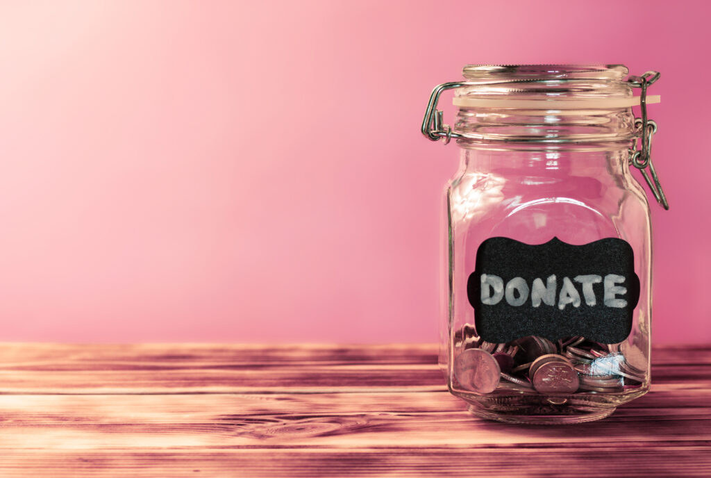 A jar has a black label that reads donate and is filled with coins.